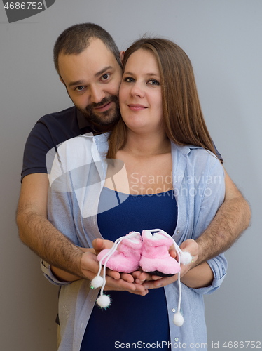 Image of pregnant couple holding newborn baby shoes