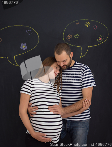 Image of pregnant couple posing against black chalk drawing board