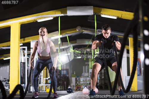 Image of sports couple doing battle ropes cross fitness exercise