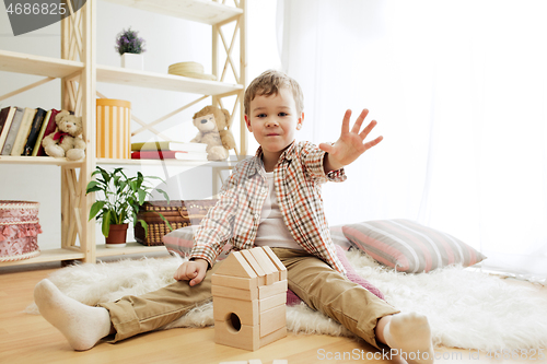 Image of Little child sitting on the floor. Pretty boy palying with wooden cubes at home