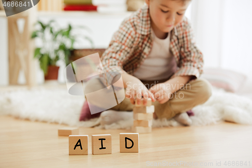 Image of Wooden cubes with word AID in hands of little boy at home.