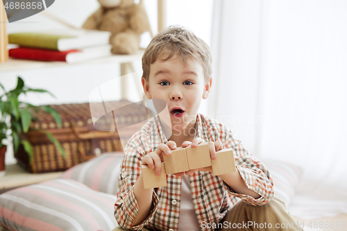 Image of Little child sitting on the floor. Pretty boy palying with wooden cubes at home