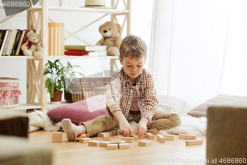 Image of Little child sitting on the floor. Pretty boy palying with wooden cubes at home