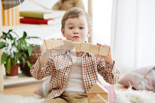 Image of Little child sitting on the floor. Pretty boy palying with wooden cubes at home