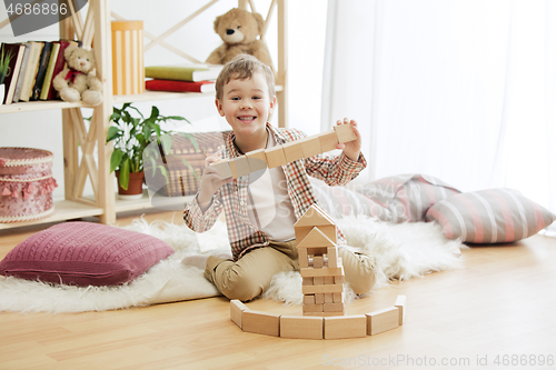 Image of Little child sitting on the floor. Pretty boy palying with wooden cubes at home