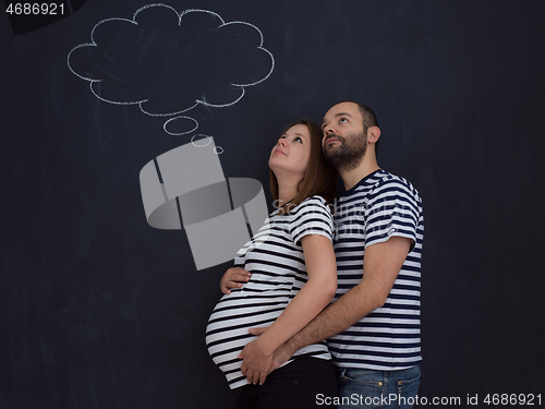 Image of pregnant couple posing against black chalk drawing board