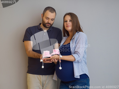 Image of pregnant couple holding newborn baby shoes