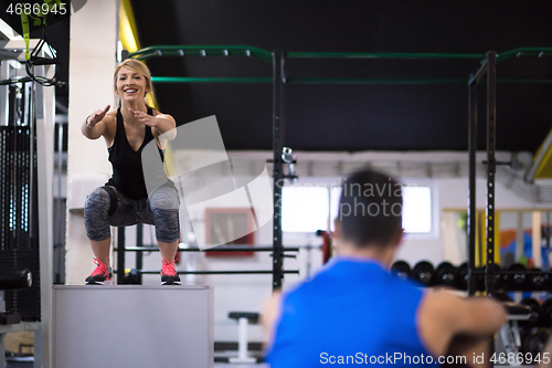 Image of woman working out with personal trainer jumping on fit box