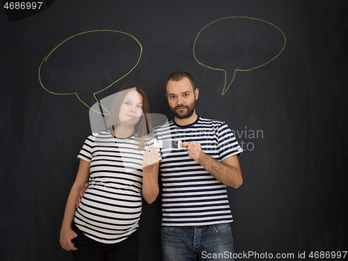 Image of pregnant couple posing against black chalk drawing board