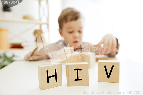 Image of Wooden cubes with word HIV in hands of little boy at home.