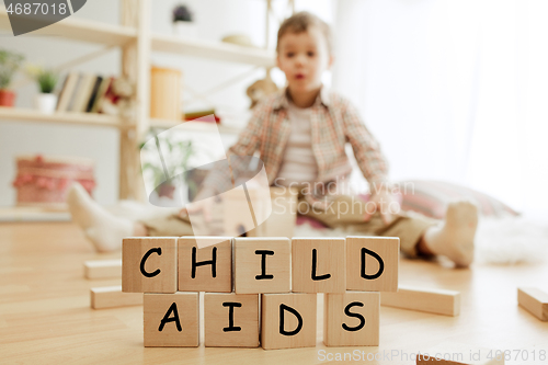 Image of Wooden cubes with words CHILD AIDS in hands of little boy at home.