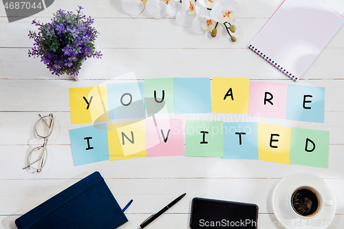 Image of YOU ARE INVITED. Message at colorful note papers on a desk background.