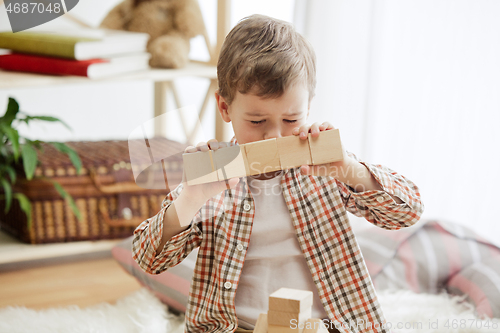 Image of Little child sitting on the floor. Pretty boy palying with wooden cubes at home