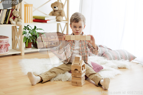 Image of Little child sitting on the floor. Pretty boy palying with wooden cubes at home