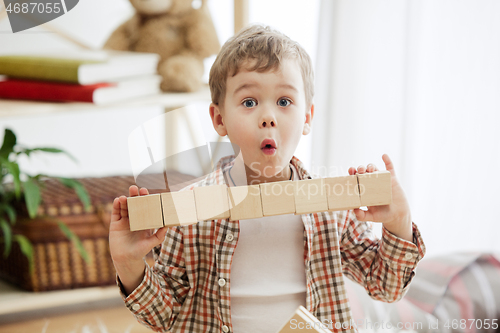 Image of Little child sitting on the floor. Pretty boy palying with wooden cubes at home