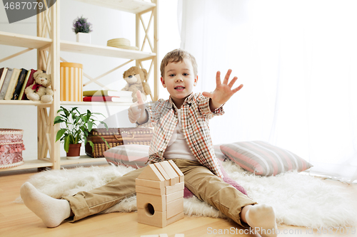 Image of Little child sitting on the floor. Pretty boy palying with wooden cubes at home