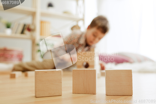 Image of Little child sitting on the floor. Pretty boy palying with wooden cubes at home