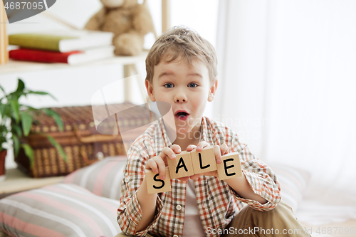 Image of Wooden cubes with word sale in hands of happy smiling little boy at home