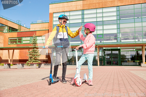 Image of happy school children with backpacks and scooters