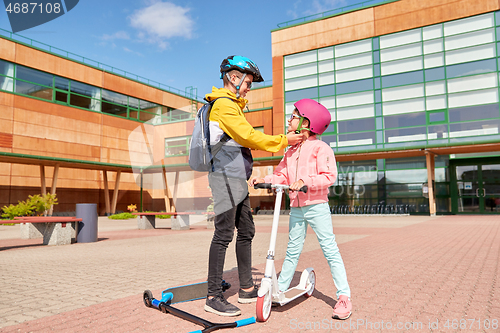 Image of school boy fastening girl\'s helmet for scooter