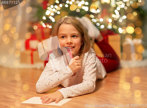 Image of smiling girl writing christmas wish list at home