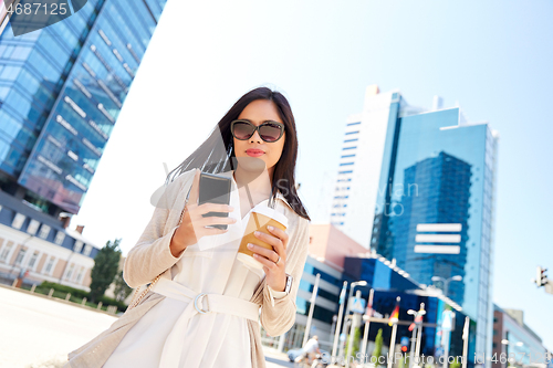 Image of smiling woman with smartphone and coffee in city