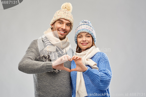 Image of happy couple in winter clothes making hand heart