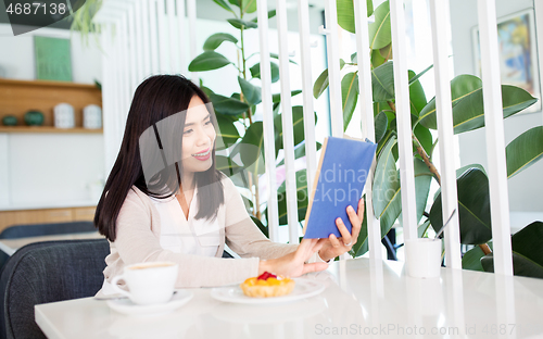 Image of woman drinking coffee and reading book at cafe