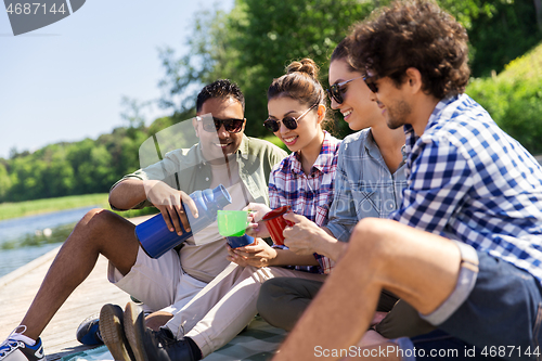 Image of happy friends drinking tea from thermos in summer