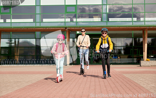 Image of happy school children with mother riding scooters