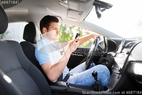 Image of man driving car and using smartphone