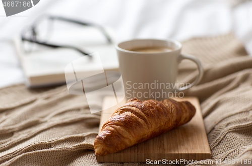 Image of croissant and cup of coffee on bed at cozy home