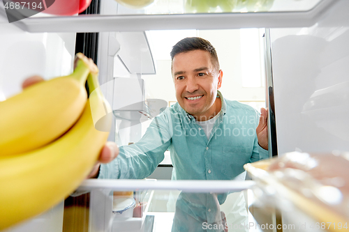 Image of man taking banana from fridge at home kitchen