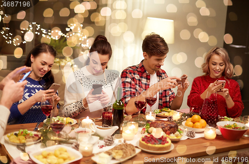Image of friends with smartphones having christmas dinner