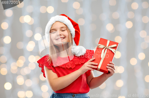 Image of pleased girl in santa hat with christmas gift
