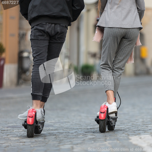 Image of Rear view of unrecognizable trendy fashinable teenagers riding public rental electric scooters in urban city environment. New eco-friendly modern public city transport in Ljubljana, Slovenia.