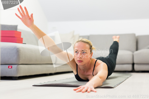 Image of Beautiful blonde woman doing home workout indoors. Woman practice yoga at home. Fit girl using workout tutorials for healthy active lifestyle. Woman using quarantine for home workouts.