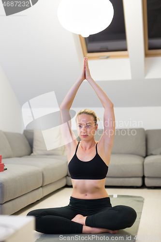 Image of Beautiful blonde woman doing home workout indoors. Woman practice yoga at home. Fit girl using workout tutorials for healthy active lifestyle. Woman using quarantine for home workouts.