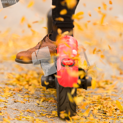 Image of Detail of fashinable hipster girl riding electric scooter in park at fall