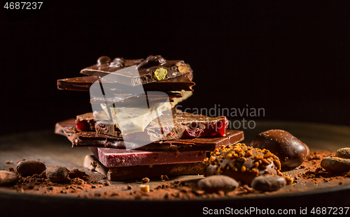 Image of Stack of assorted chocolate with cocoa and cocoa beans on black background