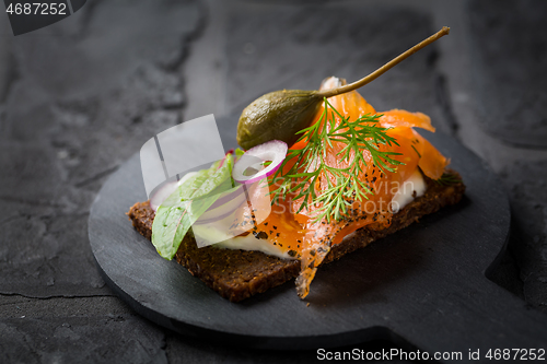 Image of Salmon open sandwich on Pumpernickel bread with vegetables, herbs and soft cheese