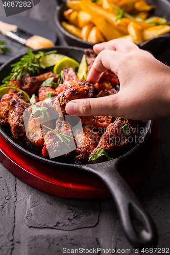 Image of Hand swiping roasted chicken wings in barbecue sauce with lime 