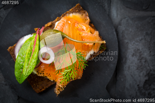 Image of Salmon open sandwich on Pumpernickel bread with vegetables, herbs and soft cheese