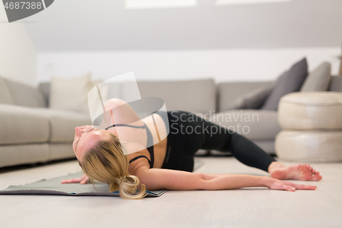 Image of Beautiful blonde woman doing home workout indoors. Woman practice yoga at home. Fit girl using workout tutorials for healthy active lifestyle. Woman using quarantine for home workouts.