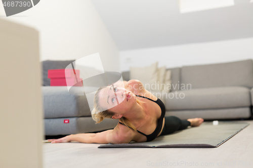 Image of Beautiful blonde woman doing home workout indoors. Woman practice yoga at home. Fit girl using workout tutorials for healthy active lifestyle. Woman using quarantine for home workouts.