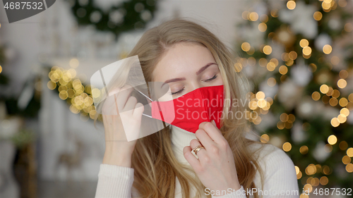 Image of Tired woman take off protective face mask while standing in festive decorated home for Christmas