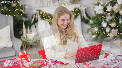 Image of Young pretty blond woman shopping online using laptop against Christmas background