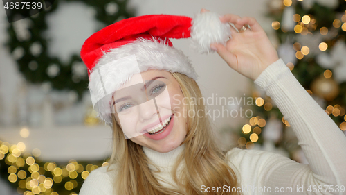 Image of Young blond beautiful smiling woman in sweater and Santa hat on christmas tree background