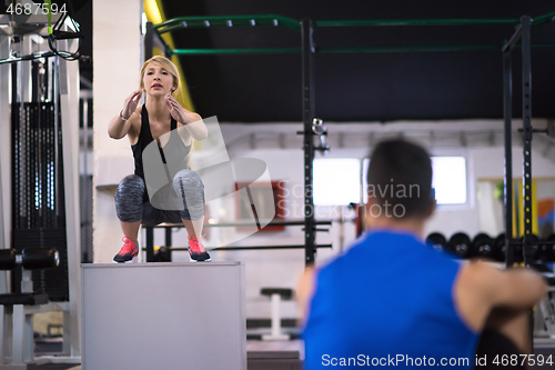 Image of woman working out with personal trainer jumping on fit box