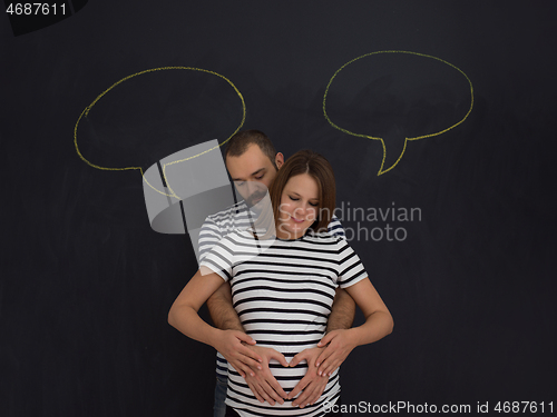 Image of pregnant couple posing against black chalk drawing board